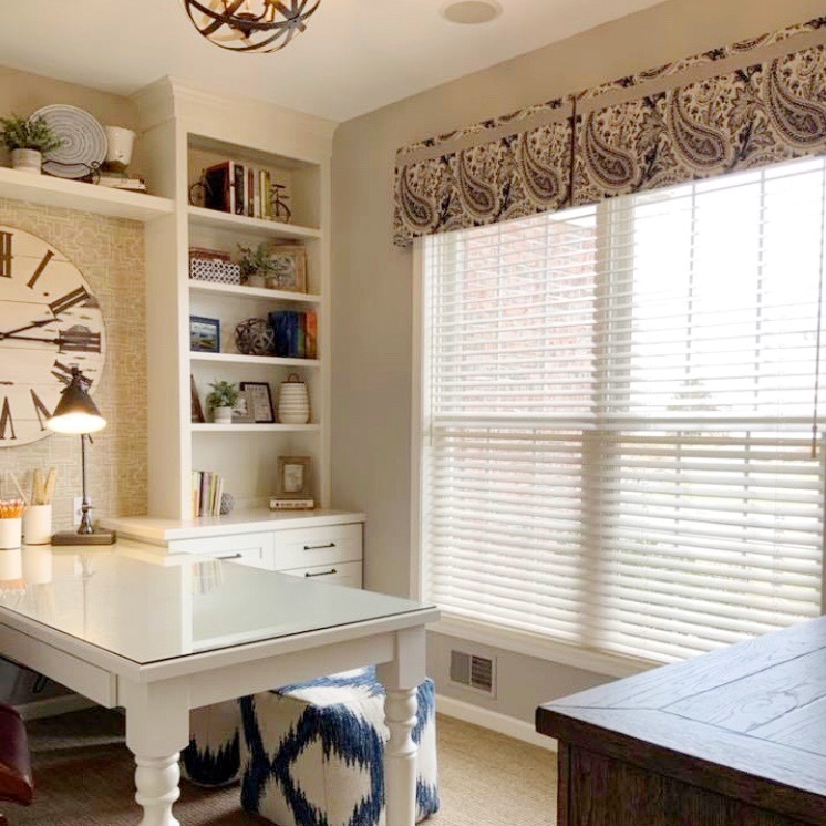 “Bright and airy home office featuring a paisley-patterned valance, white horizontal blinds for light control, and built-in shelving with decorative accents