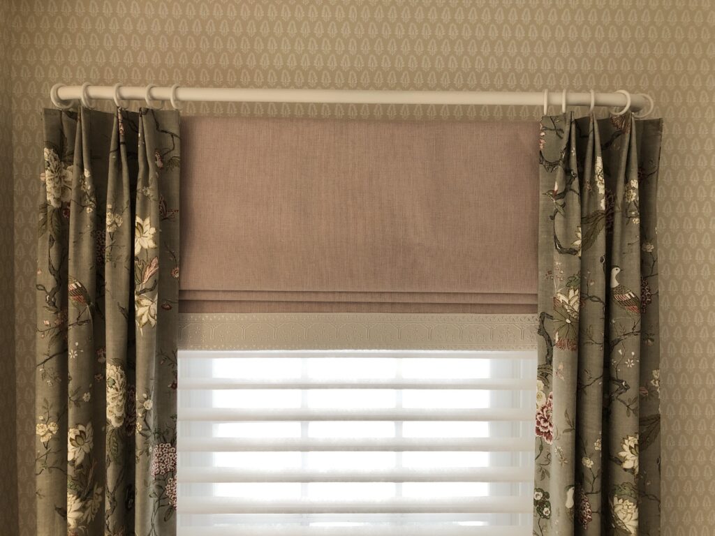Elegant window styling with a soft pink Roman shade paired with floral pinch-pleat drapery panels and light-filtering horizontal blinds