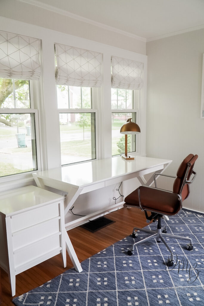 Bright and streamlined home office setup with geometric Roman shades for light control, a sleek white desk, and mid-century style office chair