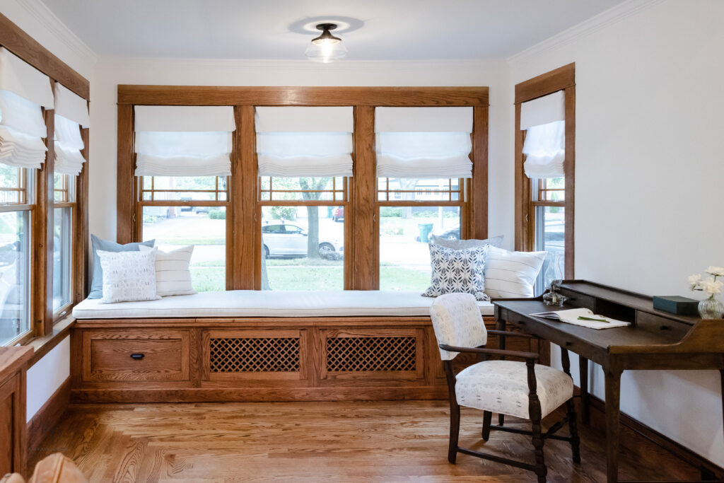 Classic built-in window seat with custom white Roman shades and wood-trimmed windows, creating a cozy and light-filled home office nook